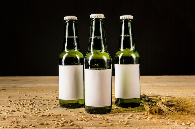 Three green beer bottles with ears of wheat on wooden surface