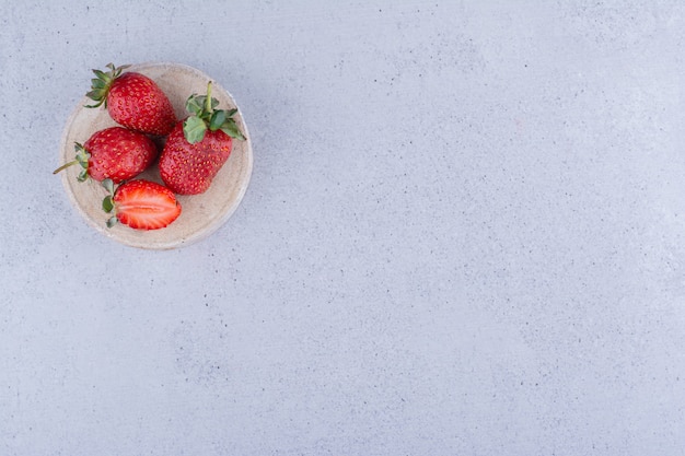 Three and a half strawberries on a piece of wood on marble background. High quality photo