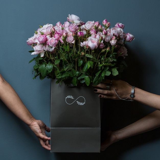 Free photo three hands holding a black basket of pink roses on wall