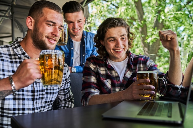 Foto gratuita tre uomini belli che guardano il calcio in un pub e bevono birra.