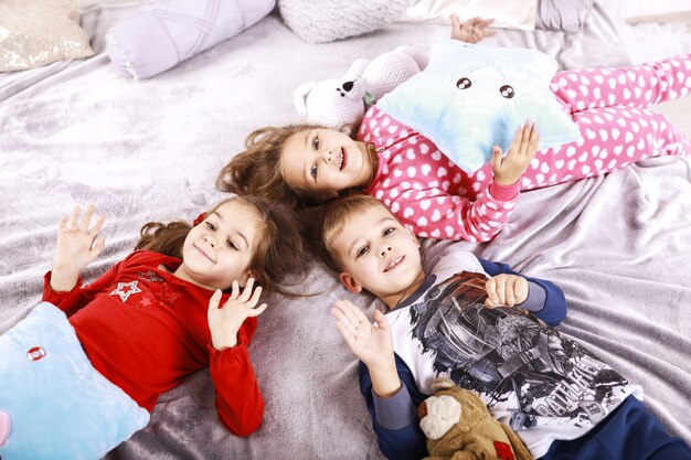 Three happy children are lying on the blanket dressed in sleepwear
