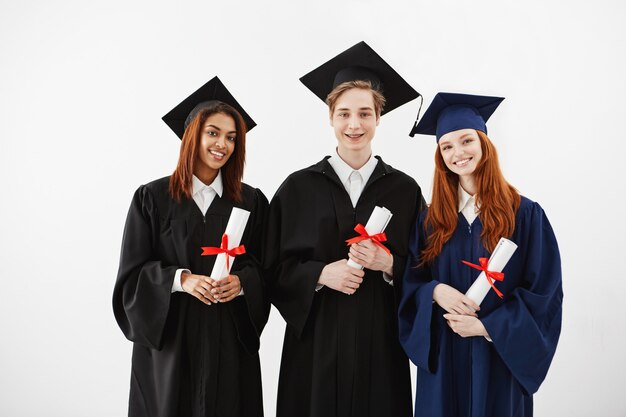 Three happy graduates smiling holding diplomas.