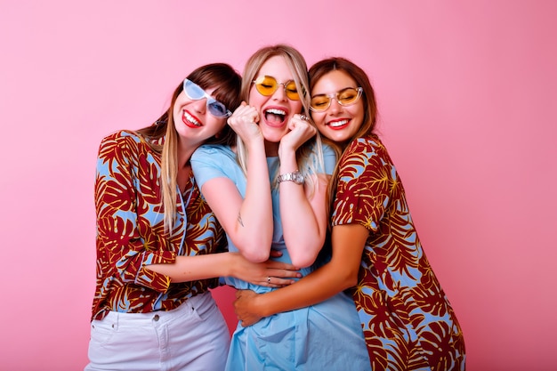 Три счастливые молодые красивые женщины, делающие селфи, веселая группа лучших друзей, стильная модная одежда с тропическим принтом и винтажные очки, розовая стена.