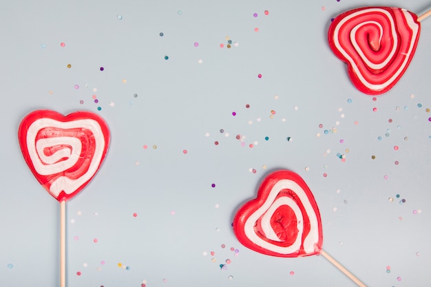 Three heart shape red lollipops on gray background with colorful confetti