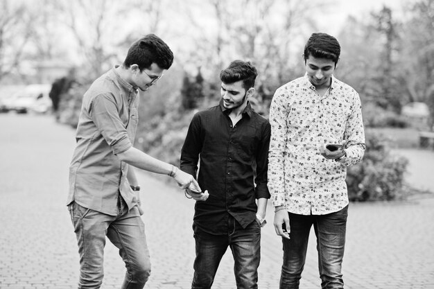 Трое индийских парней-студентов-друзей гуляют по улице и смотрят в мобильный телефон Черно-белое фото