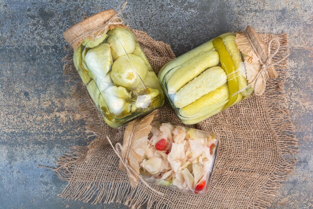 Three jars various preserved vegetables on a burlap.