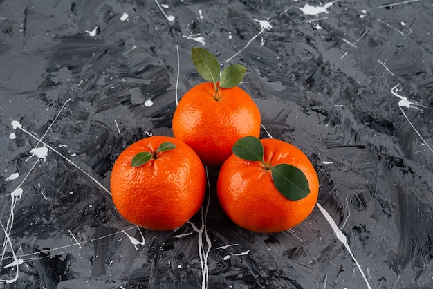 Three juicy tangerine fruits with leaves on marble surface.