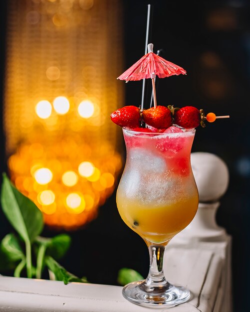 Three layered cocktail glass garnished with strawberry and cocktail umbrella