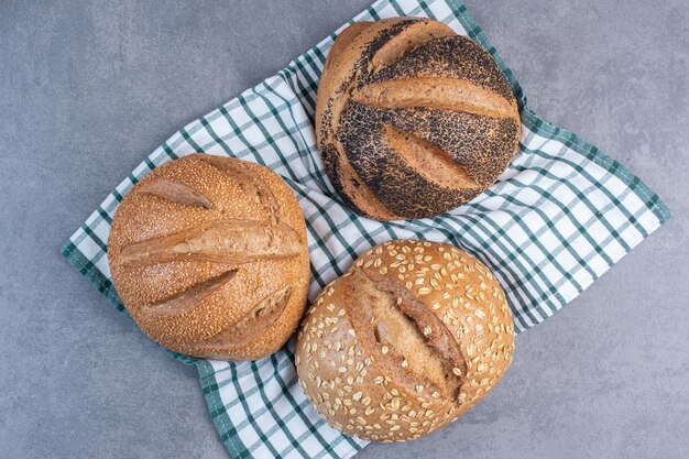 Three loaves of bread with various coatings on a towel on marble background. High quality photo