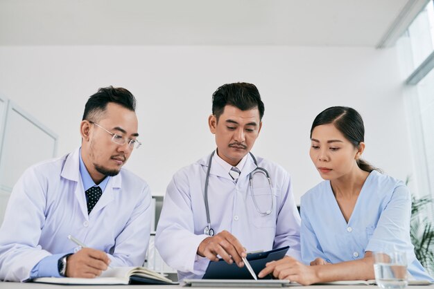 Three male and female medical professionals discussing medical history of patient