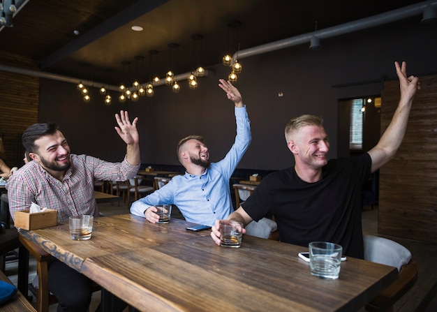 Free photo three man sitting in the restaurant greeting his friends