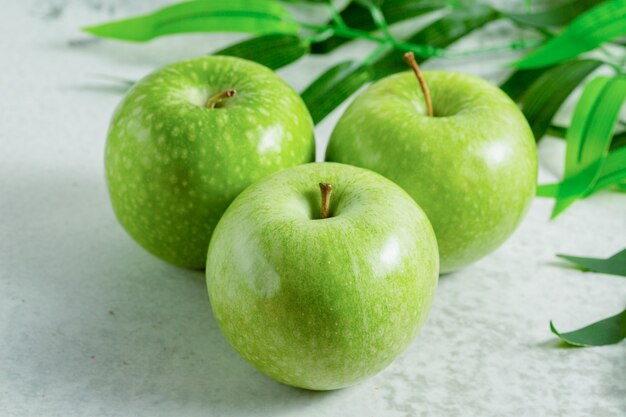 Три органических зеленых яблока на серой поверхности.
