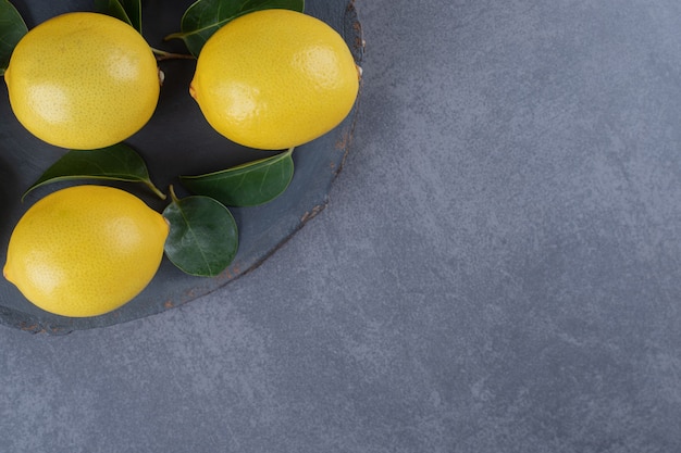 Три органических лимона на черной доске на сером фоне.