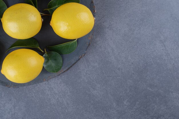 Three organic lemon on black board over grey background.