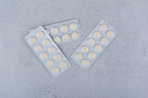 Three packs of round medicine pills on marble background. 