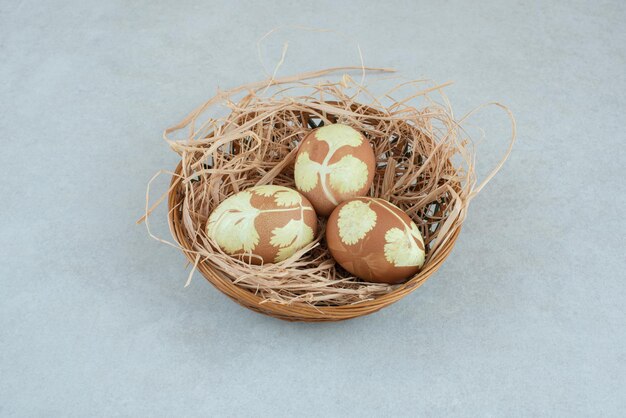 Три крашеные куриные яйца в сене на плетеной корзине.