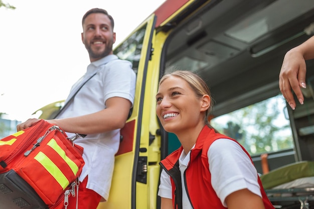 Three paramedics by the ambulance Young woman and man smiling Doctor is carrying a medical trauma bag