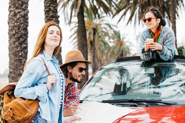 Three people standing near car with road map