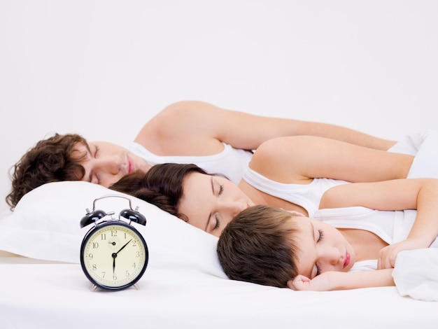Three person of the young family sleeping with alarm clock near  their  heads
