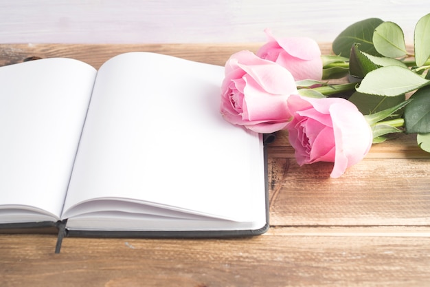 Three pink roses with an open blank diary on wooden table