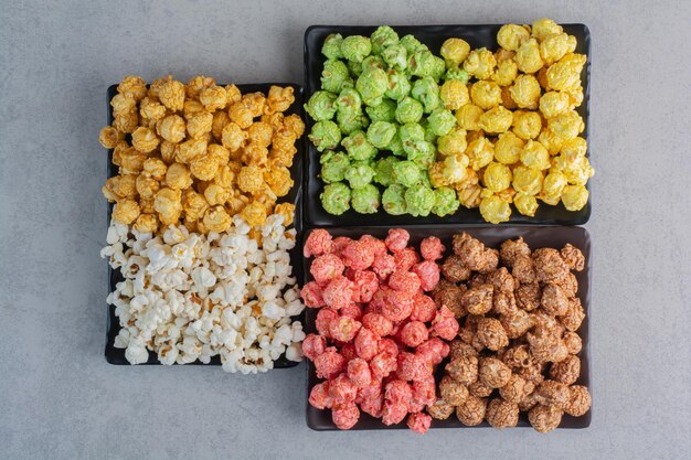 Three plates of various colored popcorn candies and simple popcorn on marble surface