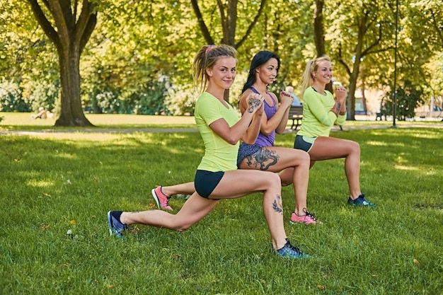 Three positive sporty female doing squats in an autumn park.