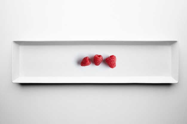 Three raspberries isolated on white ceramic plate