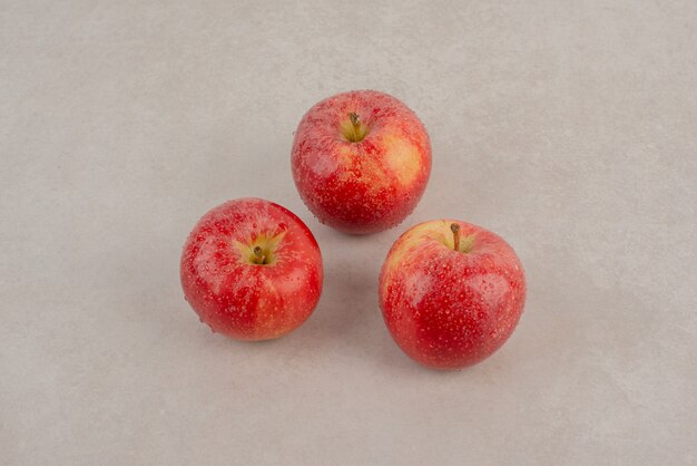 Three red apples on marble table .