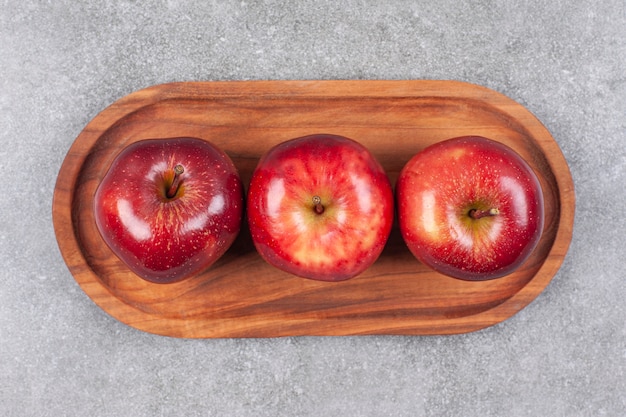 Free photo three red apples on wooden plate