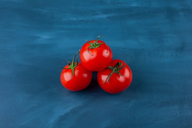 세 개의 빨간색 신선한 토마토는 파란색 표면에 배치됩니다.