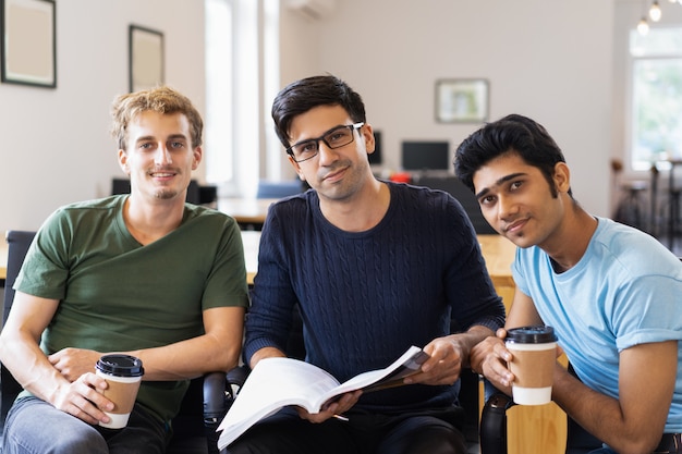 Three relaxed students studying together and drinking