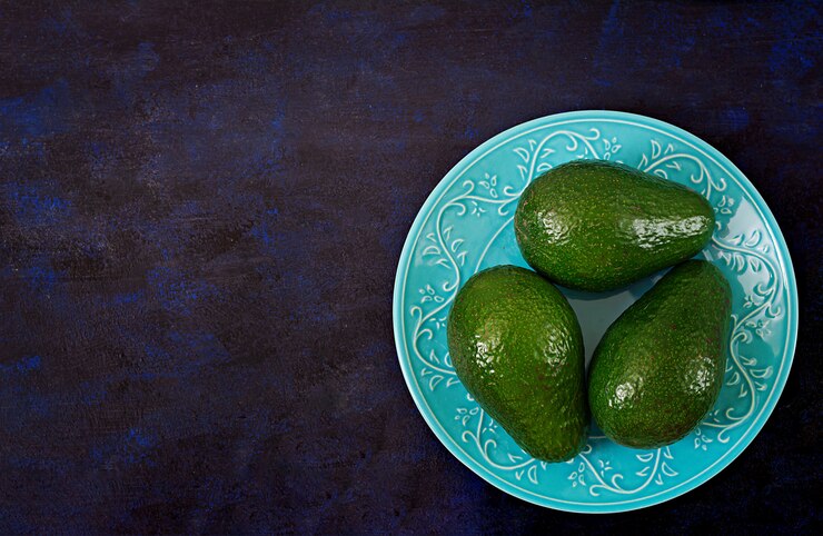 Free Photo three ripe avocados on a dark table. healthy food concept. top view