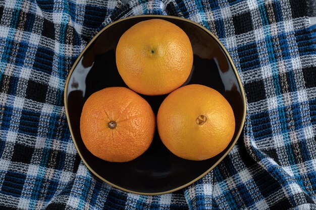 Three ripe oranges on black plate with tablecloth. 