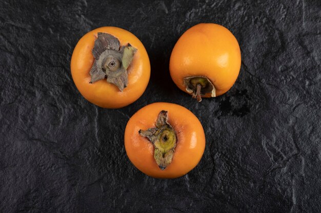 Three ripe persimmon fruits placed on black surface