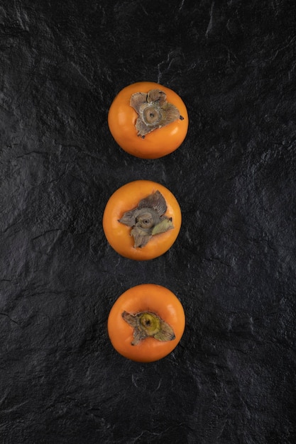 Три спелых плода хурмы на черной поверхности
