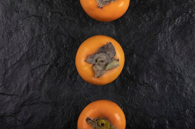 Three ripe persimmon fruits placed on black surface