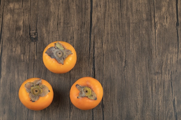 Free photo three ripe persimmon fruits placed on wooden surface