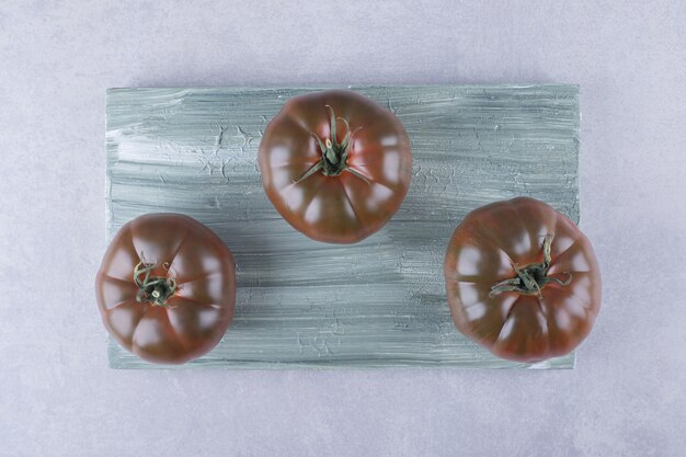 Three ripe tomatoes on wooden board. 