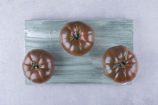 Три спелых помидора на деревянной доске.
