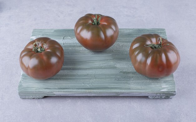 Three ripe tomatoes on wooden board. 