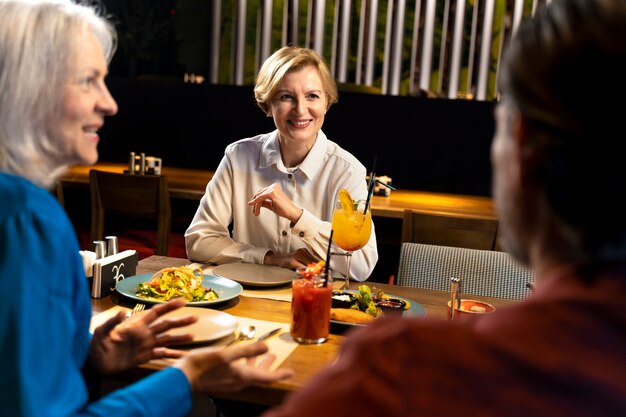 Three senior friends talking at a restaurant while eating and drinking