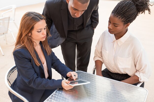 Three serious young businesspeople watching data on pc tablet