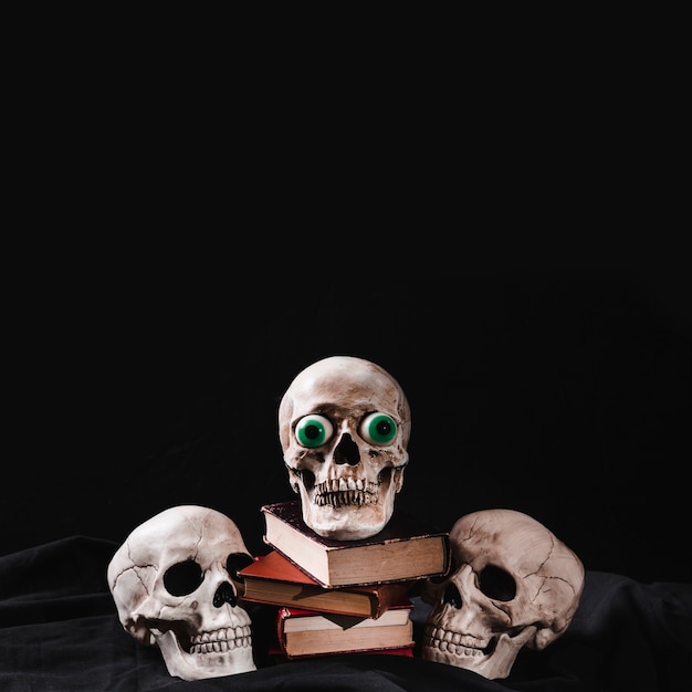 Three skulls and pile of books on black background