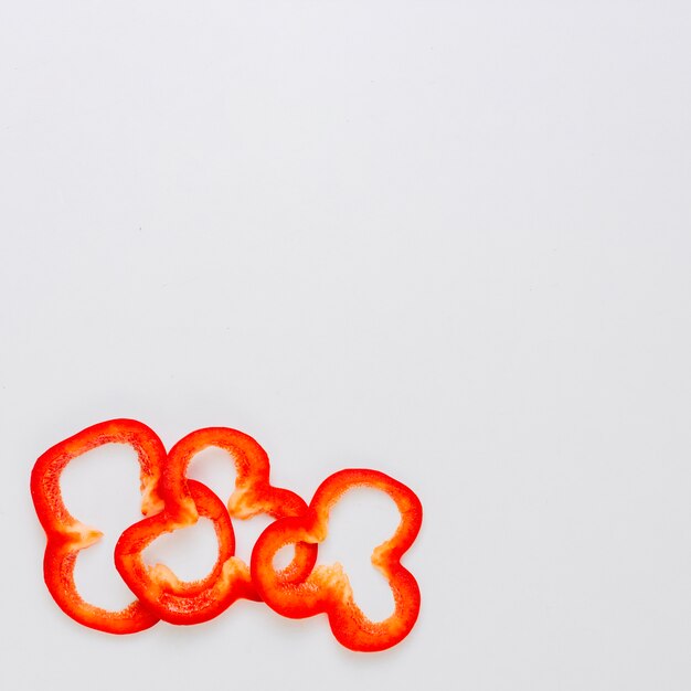 Three slices of red bell pepper on the corner of the white background