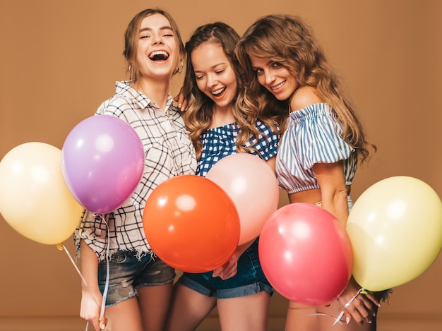 Three smiling beautiful women in checkered shirt summer clothes. girls posing. models with colorful balloons. having fun, ready for celebration birthday