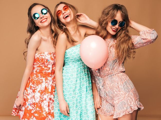 Три улыбающиеся красивые женщины в клетчатой рубашке летней одежды. Девочки позируют. Модели с разноцветными шарами в солнцезащитные очки. Веселимся, готовимся к празднованию дня рождения или праздничной вечеринки