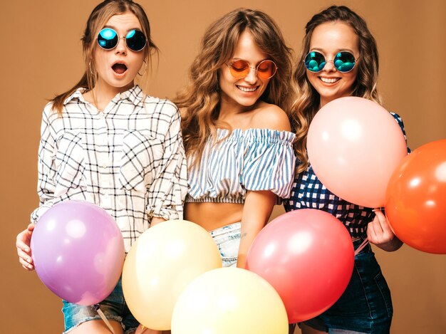 Three smiling beautiful women in checkered shirt summer clothes. Girls posing. Models with colorful balloons in sunglasses. Having fun, ready for celebration birthday