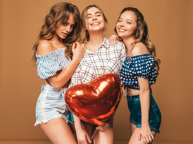 Three smiling beautiful women in checkered shirt summer clothes. Girls posing. Models with heart shape balloon. Ready for celebration Valentine's Day