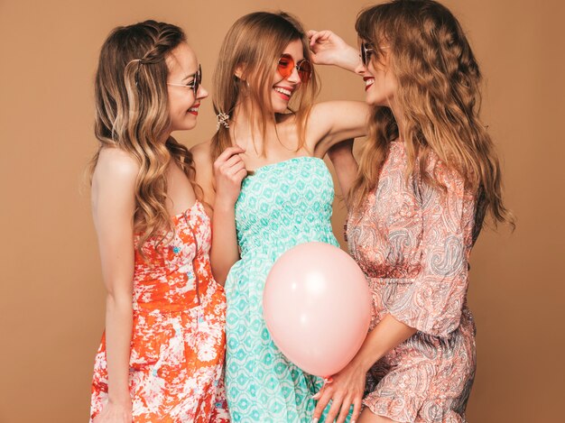 Three smiling beautiful women in summer dresses. Girls posing. Models with colorful balloons. Having fun, ready for celebration birthday or holiday party