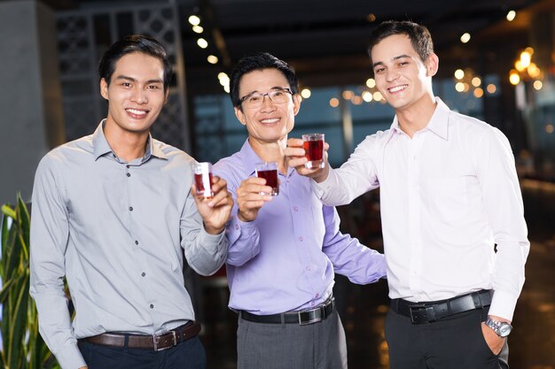 Three Smiling Men Raising Glasses in Bar